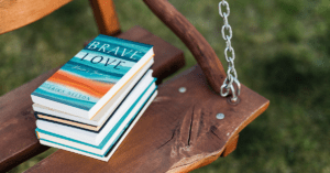 Stack of books on a wooden swing with the book Brave Love: Alexia's Journey on top of the stack.