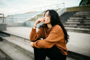 An Asian woman sitting on concrete steps, pondering something.