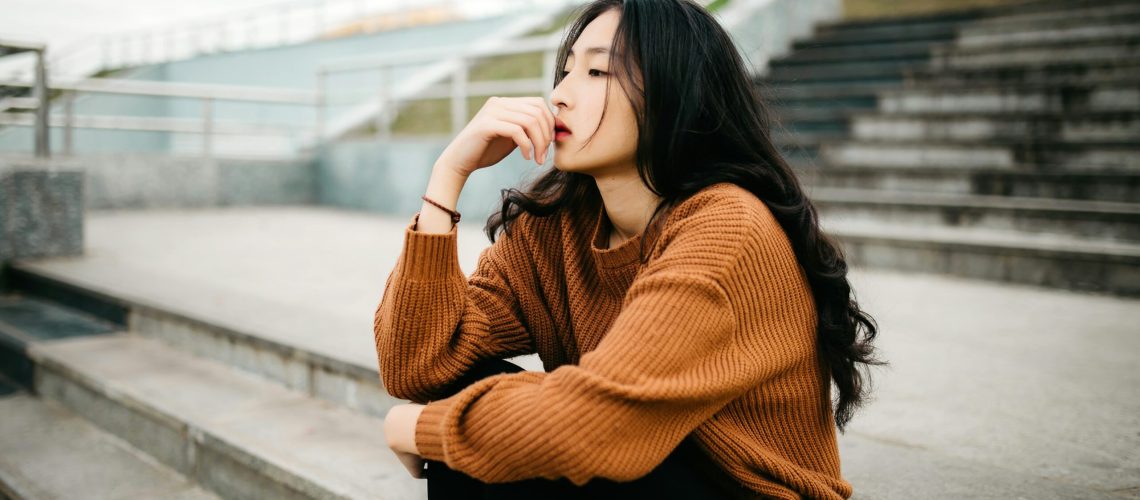 An Asian woman sitting on concrete steps, pondering something.